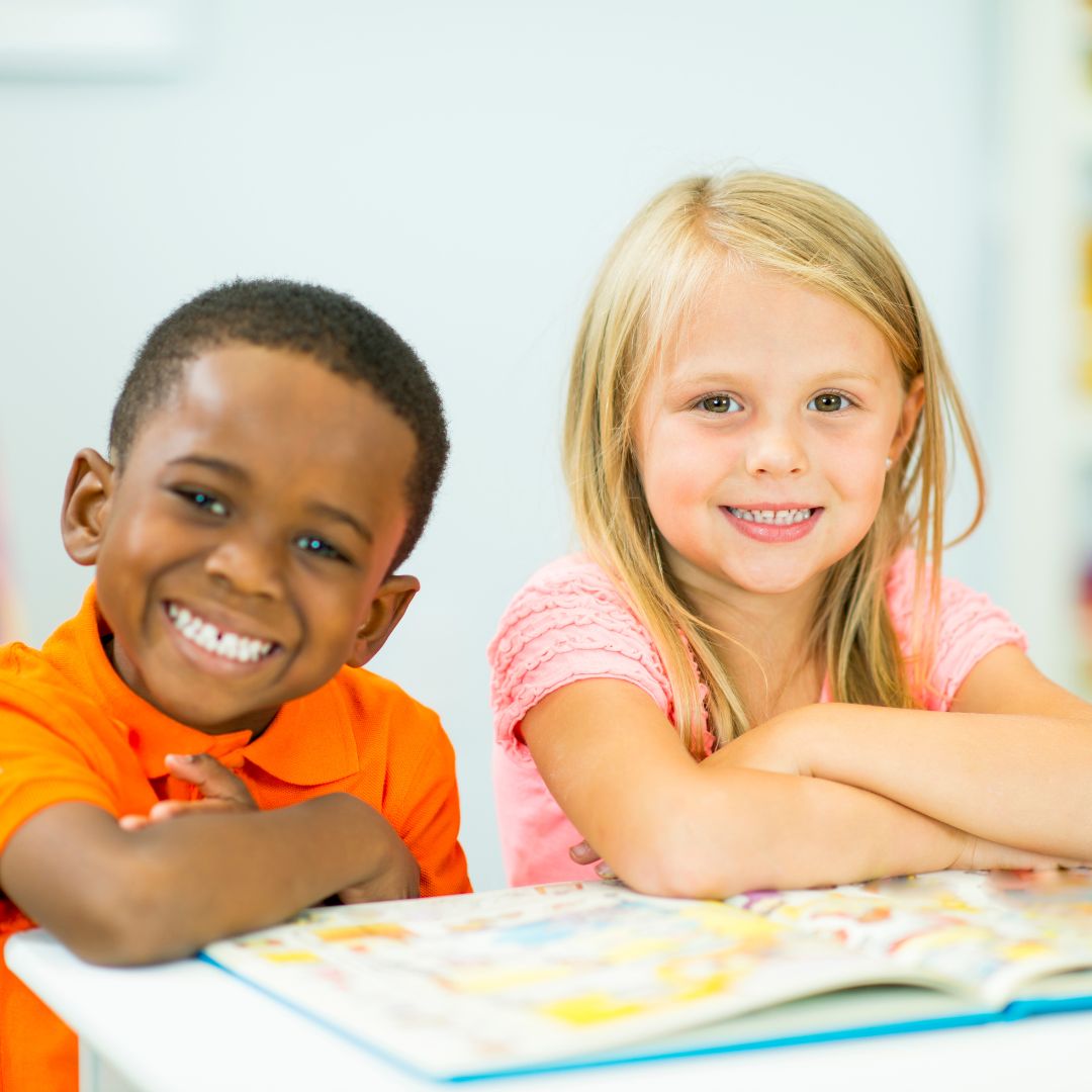 two smiling preschoolers looking up from a book