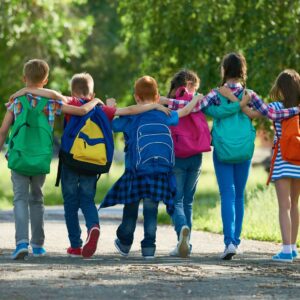children locking arms walking down a park trail with backpacks