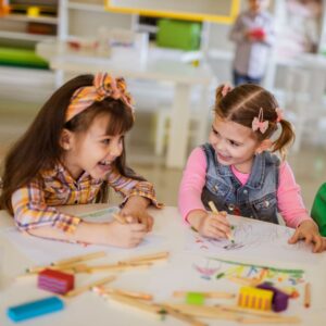 Two young girls drawing and looking happy. 