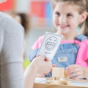 Teacher holding out a piece of paper that says "excited" to a young girl. 