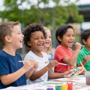 A group of diverse children laughing while painting outside.